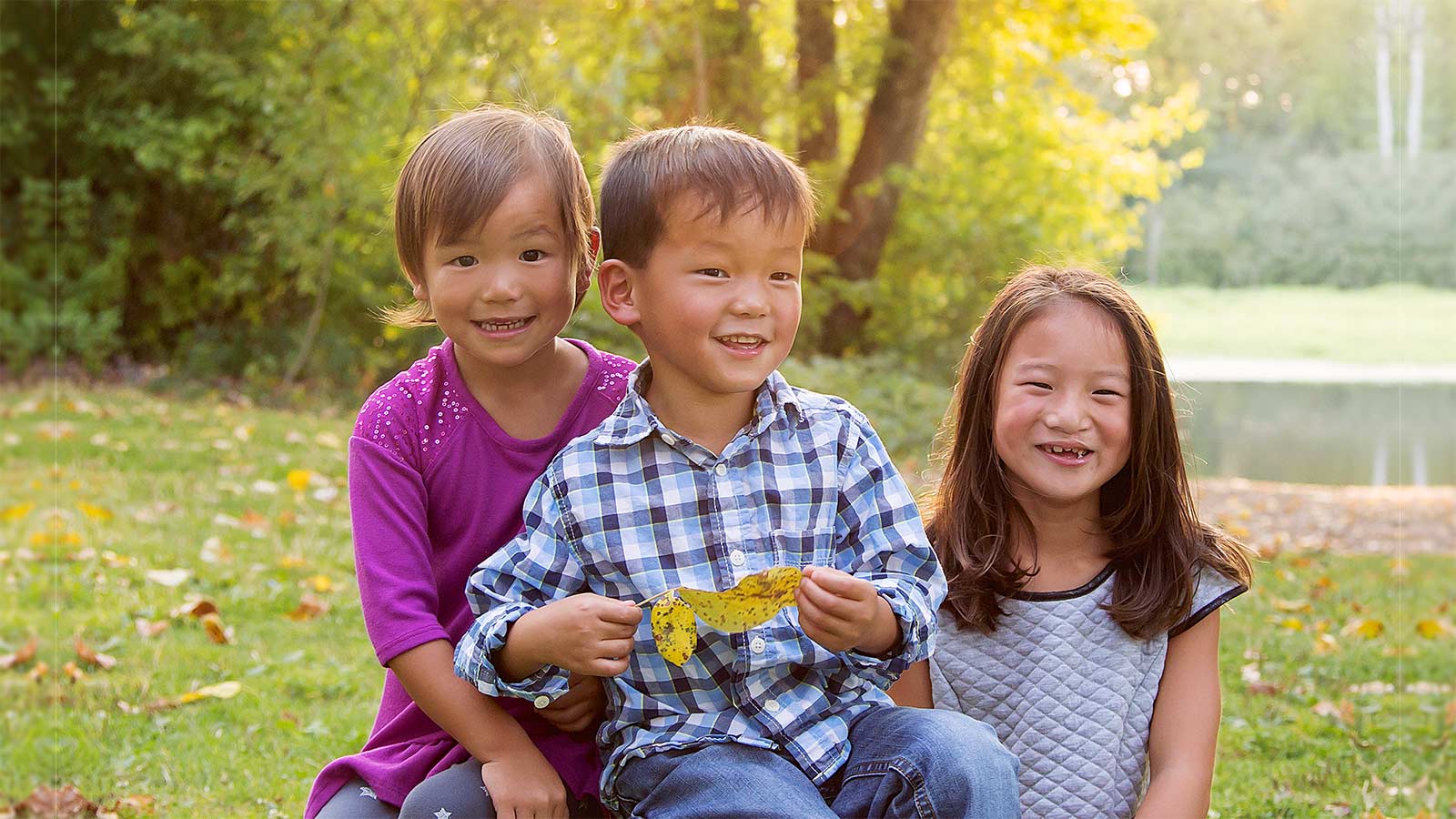 three adopted siblings sitting together in a sunny field