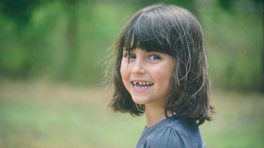 stock photo girl adopted from bulgaria with short brown hair and bangs smiling over her shoulder