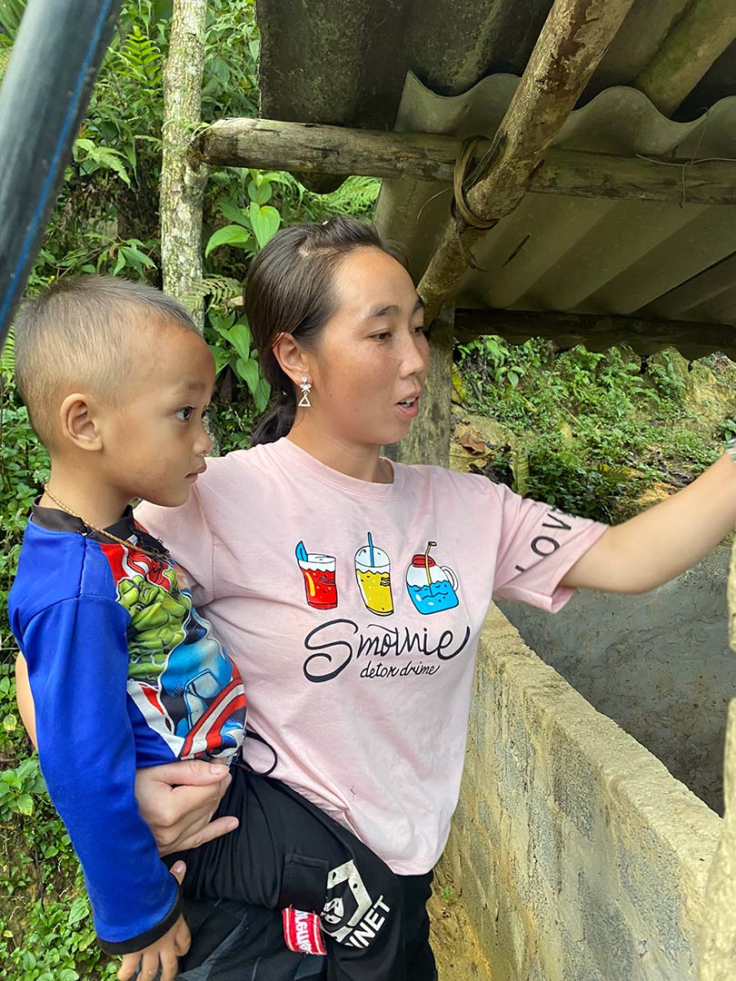 A mom in Vietnam holds her son and stands near their pigsty