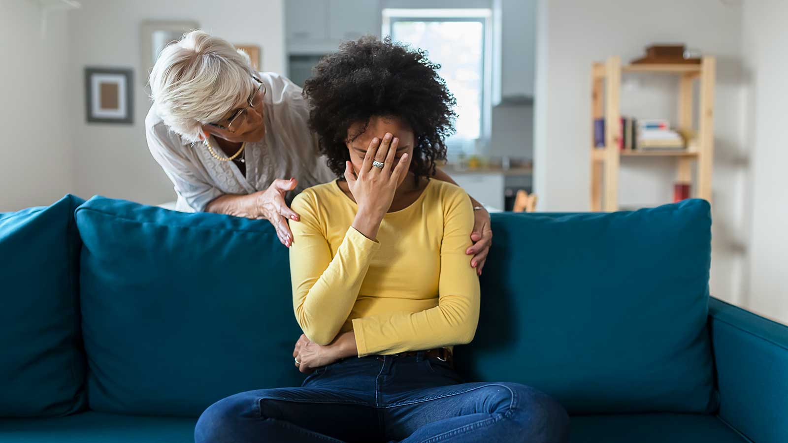 Older white woman comforting younger Black woman with her face in her hands