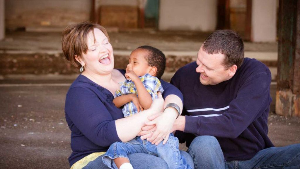 Mom and dad laughing and playing with adopted son.