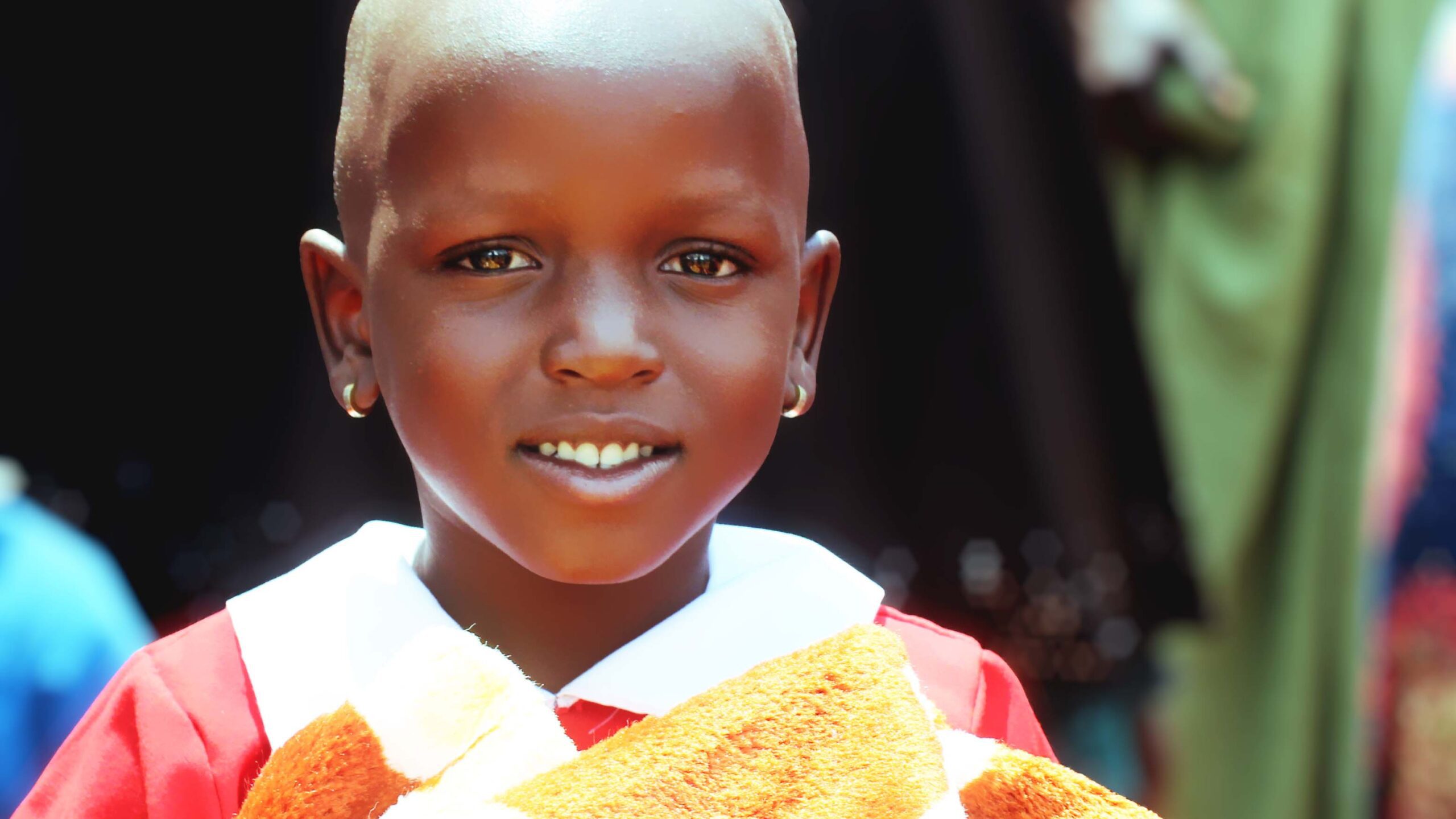 Little girl in a red dress holds a yellow blanket close and smiles