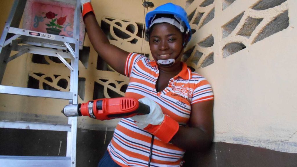 Haitian woman holding drill on ladder