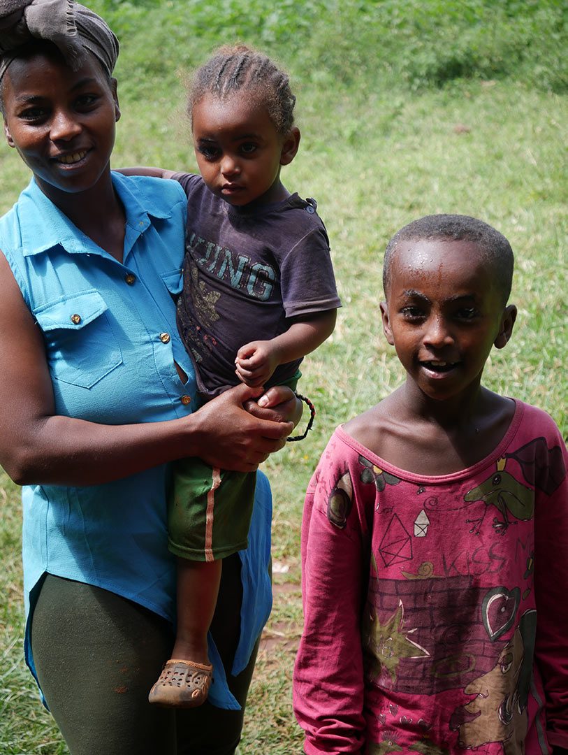 A mom holds a toddler and smiles next to her older son, medical care